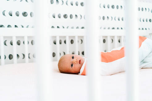View through a crib of a newborn baby girl laying down - CAVF78910