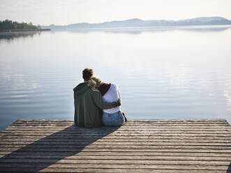 Romantic couple sitting on jetty at the lake - PNEF02565