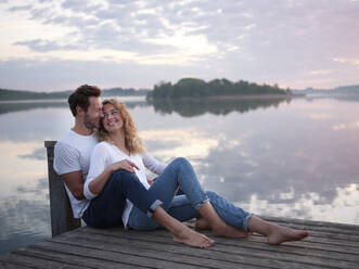 Romantic couple sitting on jetty at the lake - PNEF02566