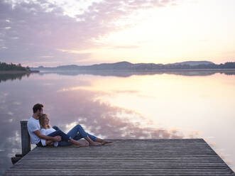 Romantic couple sitting on jetty at the lake - PNEF02568