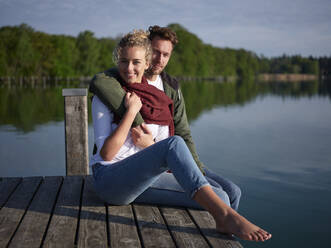 Romantic couple sitting on jetty at the lake - PNEF02580