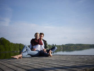 Romantisches Paar auf dem Steg am See sitzend - PNEF02581