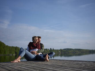 Romantisches Paar auf dem Steg am See sitzend - PNEF02582