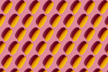 Muster aus gelben Plastikmaiskolben vor rosa Hintergrund - GEMF03521