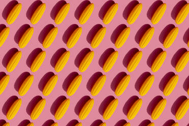 Pattern of yellow plastic corn cobs against pink background - GEMF03521