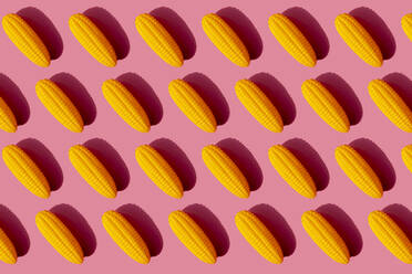 Muster aus gelben Plastikmaiskolben vor rosa Hintergrund - GEMF03522