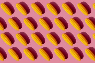 Pattern of yellow plastic corn cobs against pink background - GEMF03522