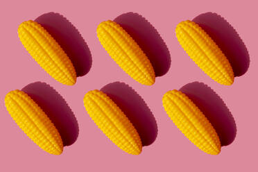 Studio shot of six plastic corn cobs against pink background - GEMF03524