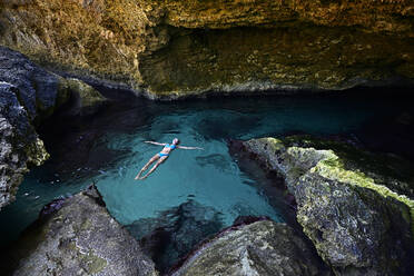 Frau schwebt auf klarem Wasser in einer Grotte - ECPF00867