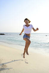 Beautiful woman running and jumping for joy on the beach - ECPF00871