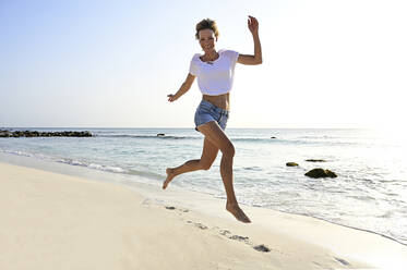 Beautiful woman running and jumping for joy on the beach - ECPF00872