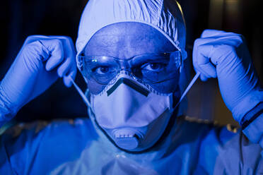 Doctor wearing protective clothing, putting on face mask - CJMF00290