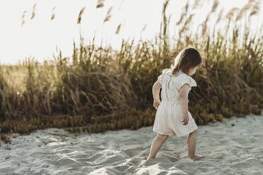 Hinter Ansicht des jungen Kleinkindes Mädchen zu Fuß am Sandstrand bei Sonnenuntergang - CAVF78940