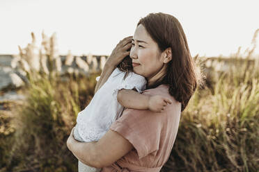 Mid Ansicht der glücklichen Mutter umarmt junge Kleinkind am Strand bei Sonnenuntergang - CAVF78942