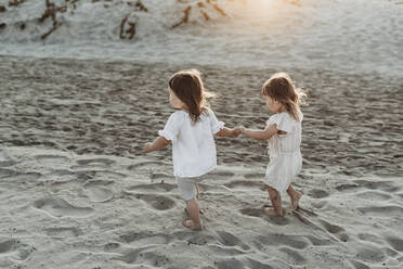 Side view of young toddler girls holding hands and walking at beach - CAVF78946