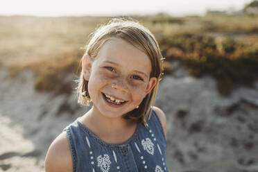 Portrait of young school age girl with freckles smiling on beach - CAVF78952