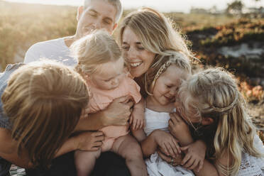 Lifestyle close up of family with young sisters sitting on beach - CAVF78956