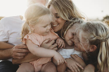 Lifestyle close up of family with young sisters sitting on beach - CAVF78960