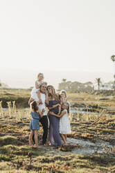 Lifestyle portrait of family with young girls smiling at beach sunset - CAVF78961