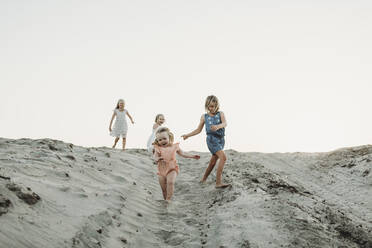 Vier junge Schwestern laufen im Sand am Strand bei Sonnenuntergang - CAVF78967
