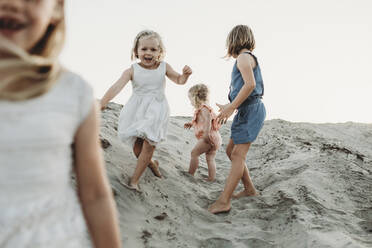 Vier junge Schwestern laufen und spielen im Sand am Strand bei Sonnenuntergang - CAVF78968