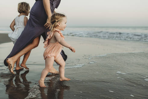 Side view of toddler girl running into the ocean at sunset - CAVF78969
