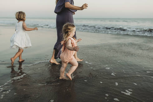 Behind view of young family walking towards the ocean at sunset - CAVF78970