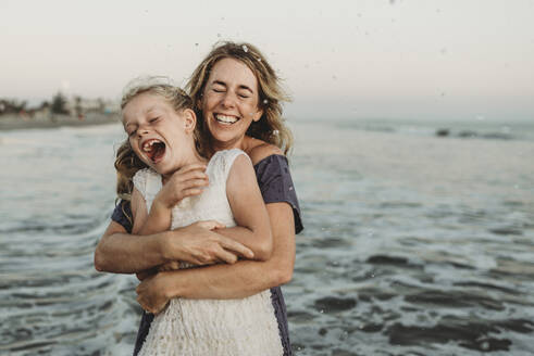 Mutter umarmt junges Mädchen mit Sommersprossen im Meer - CAVF78971