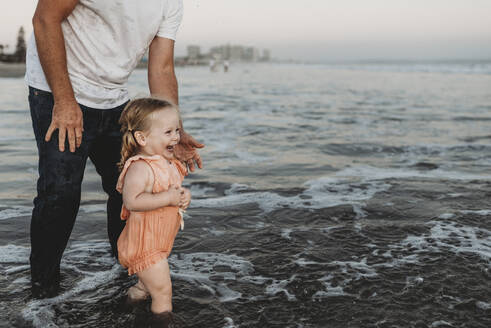 Kleines Mädchen planscht mit Vater bei Sonnenuntergang im Meer - CAVF78972