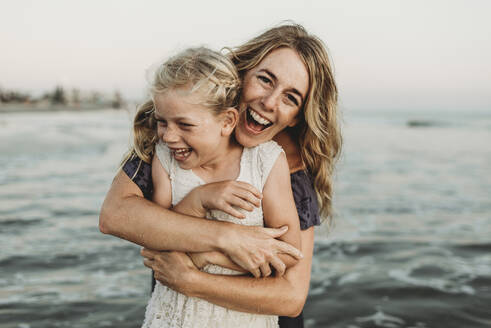 Mutter umarmt junges Mädchen mit Sommersprossen im Meer lachend - CAVF78973