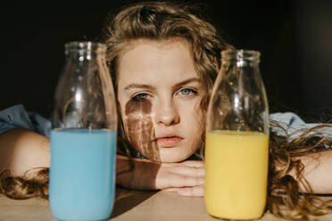 Portrait of blond young woman at home with colored bottles - TCEF00434