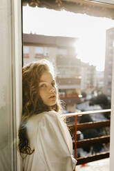 Porträt einer blonden jungen Frau an der Balkontür im Gegenlicht - TCEF00448