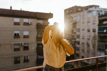 Porträt einer schönen jungen Frau auf einem Balkon bei Sonnenuntergang - TCEF00455