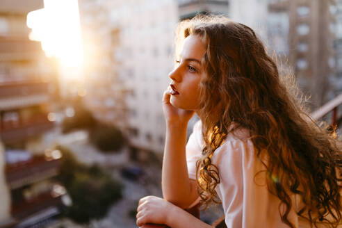 Porträt einer schönen jungen Frau auf einem Balkon bei Sonnenuntergang - TCEF00458