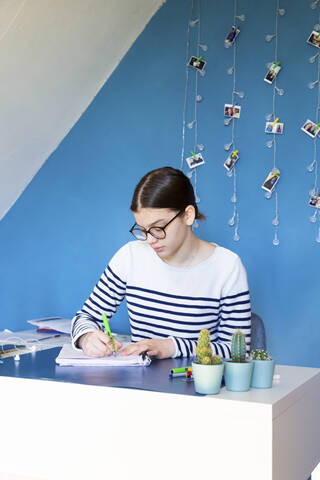 Porträt eines Mädchens, das zu Hause am Schreibtisch sitzt und Hausaufgaben macht, lizenzfreies Stockfoto