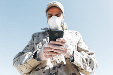 Soldat mit Gesichtsmaske im Notfalleinsatz, mit Smartphone - JCMF00568