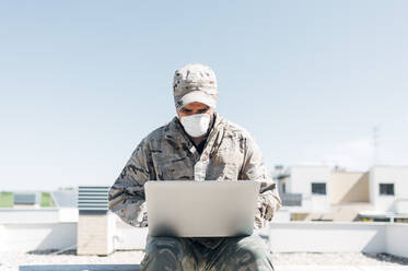 Soldat mit Gesichtsmaske im Notfalleinsatz, mit Laptop - JCMF00569