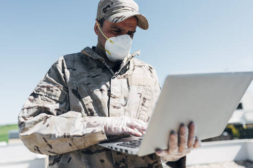 Soldat mit Gesichtsmaske im Notfalleinsatz, mit Laptop - JCMF00570