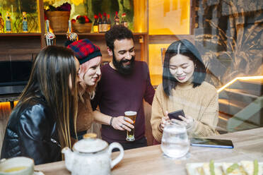 Freunde treffen sich in einer trendigen Bar und schauen auf ihr Smartphone - DGOF00678