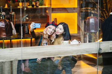 Zwei Freundinnen sitzen im Restaurant und nehmen sich ein Smartphone - DGOF00688