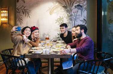 Freunde beim Abendessen in einem schicken Restaurant, die mit ihrem Smartphone Selfies machen - DGOF00722