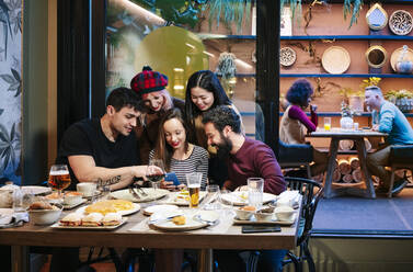 Freunde beim Abendessen in einem schicken Restaurant, die auf ihr Smartphone schauen - DGOF00723