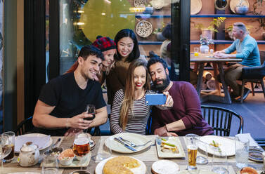 Freunde beim Abendessen in einem schicken Restaurant, die mit ihrem Smartphone Selfies machen - DGOF00725