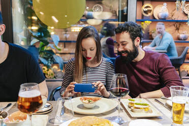 Woman taking smartphone pictures of food at a dinner with friends in a restaurant - DGOF00727