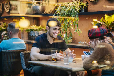 Mann und Frau, die in einem Restaurant etwas trinken, sich unterhalten und ein Smartphone benutzen - DGOF00761