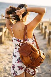 Rückansicht einer jungen Frau mit Ledertasche, die am Strand spazieren geht - MPPF00752