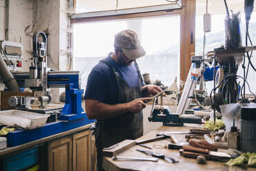 Handwerker, der in seiner Werkstatt Messer herstellt und die Klinge untersucht - DGOF00790