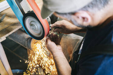 Handwerker, der in seiner Werkstatt Messer herstellt und die Klinge schärft - DGOF00796