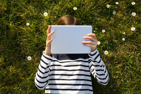 Kleines Mädchen liegt auf einer Blumenwiese und versteckt sein Gesicht hinter einem digitalen Tablet - LVF08768