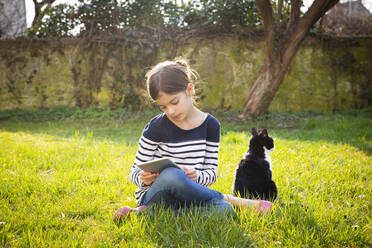 Little girl sitting on a meadow using digital tablet - LVF08769